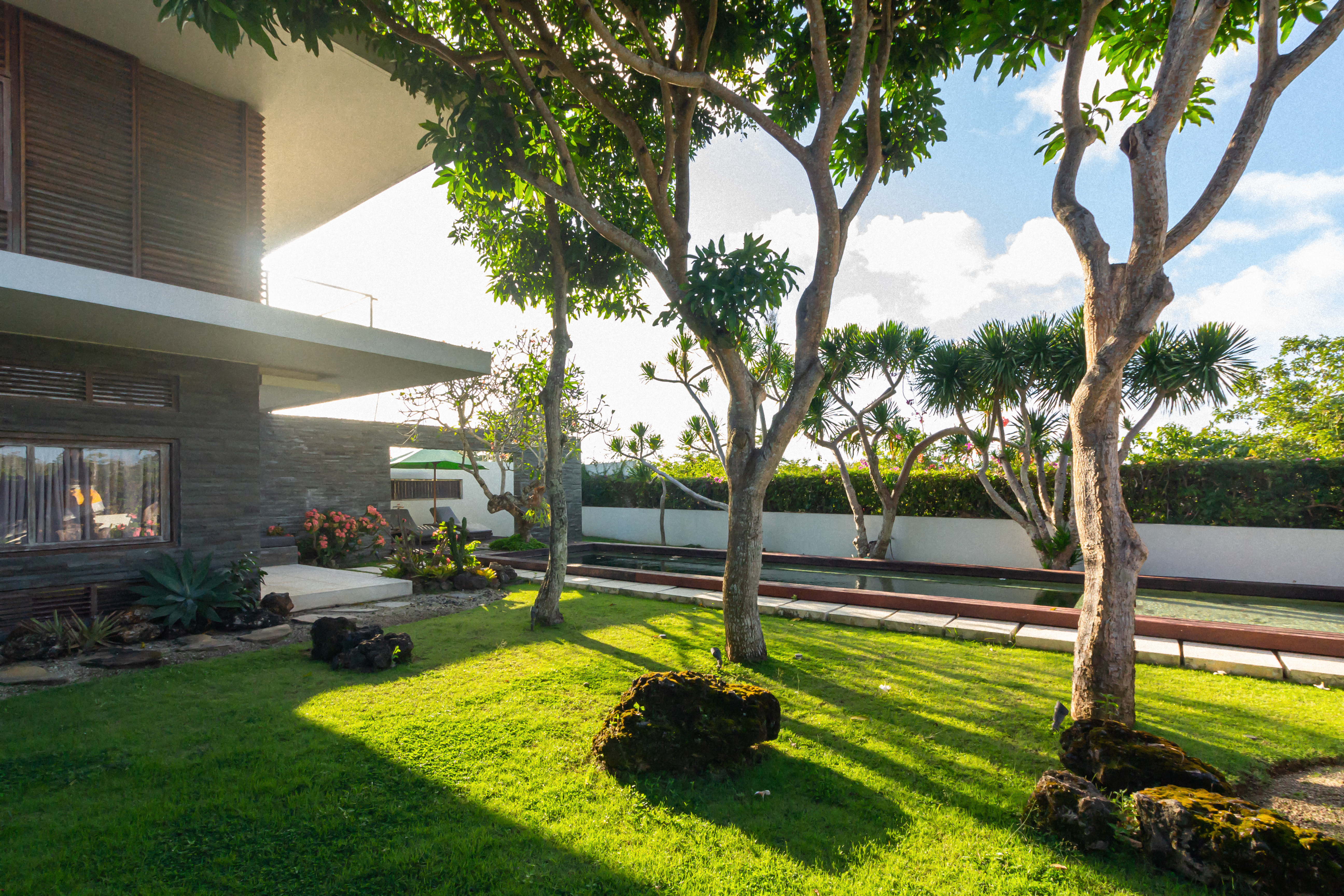 large house with a lush green lawn and a pool. The house is surrounded by trees and bushes, creating a peaceful and serene atmosphere